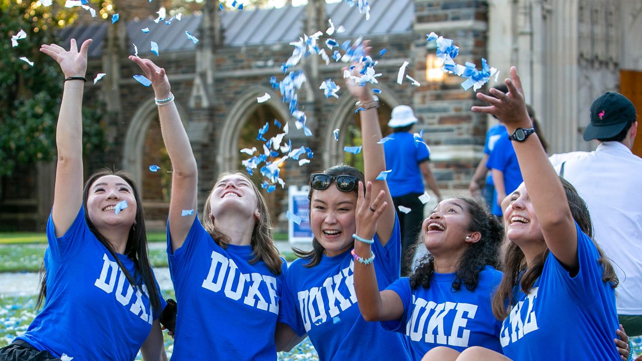 Students wearing "Duke" shirts throwing confetti in the air in front of Duke Chapel